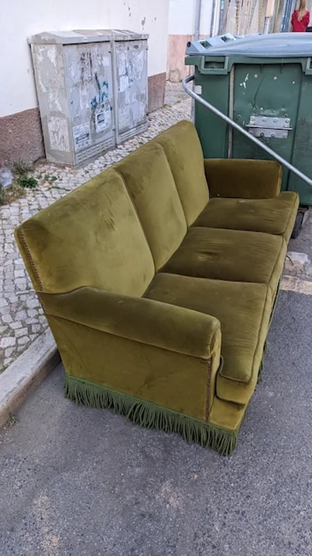 Stara materiałowa sofa obok kosza na śmieci obok chodnika