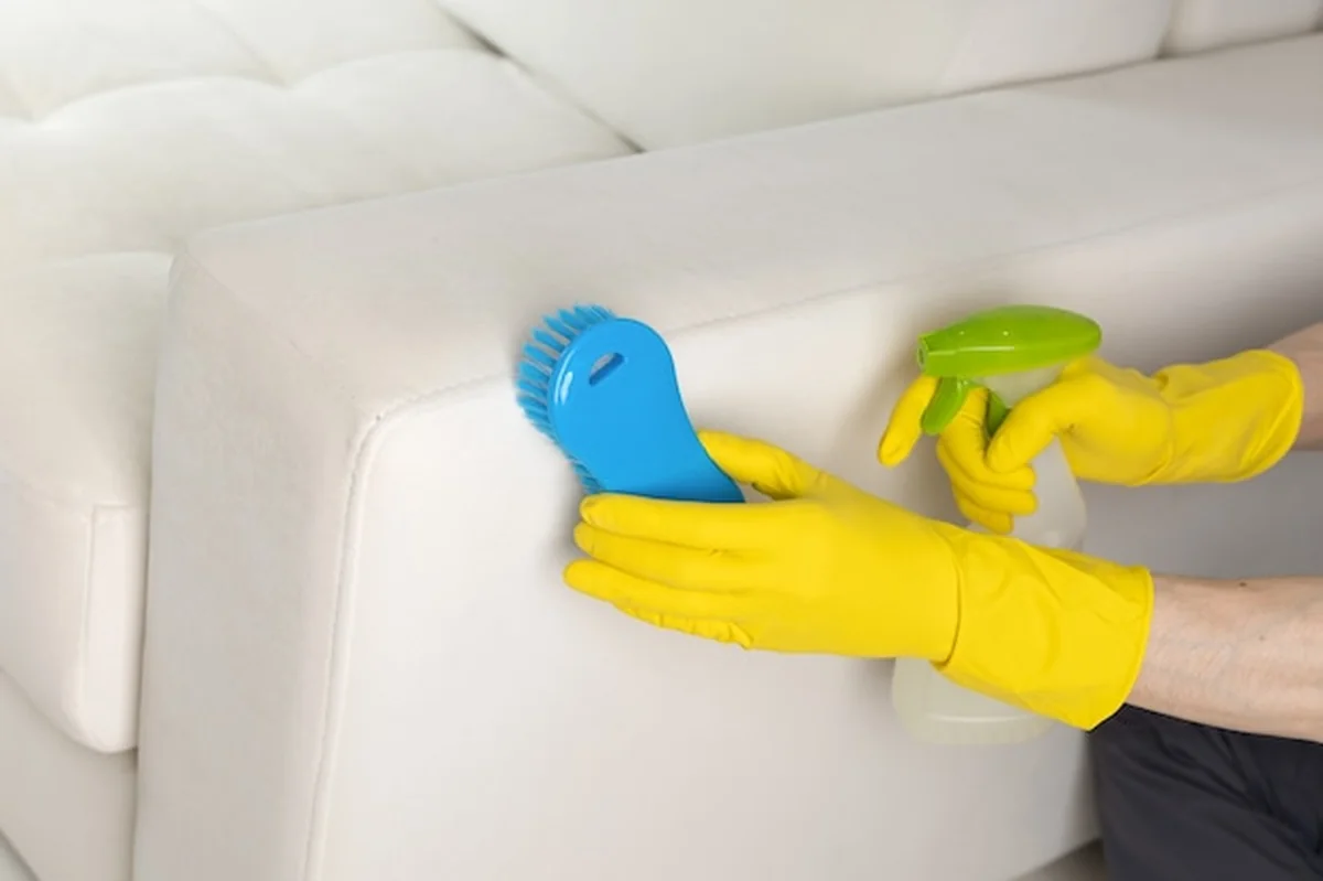 Mężczyzna czyści plamę na kanapie za pomocą spryskiwacza i pędzla