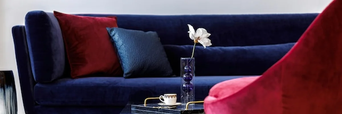 Czerwone poduszki na granatowej kanapie w nowoczesnym salonie z niebieską sofą i czerwonym fotelem