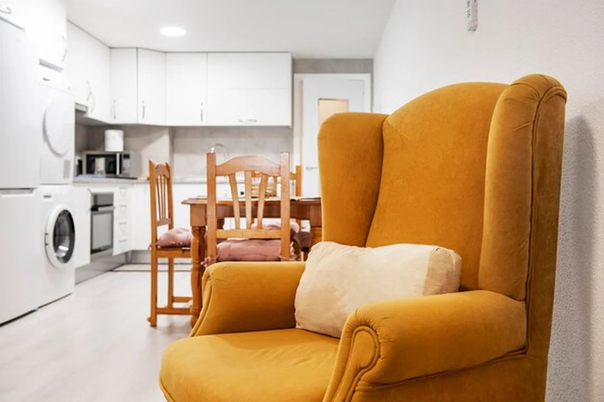 Pokój dzienny z jasnobrązową sofą, poduszkami i fotelem, telewizorem, stolikiem kawowym i sztucznymi roślinami