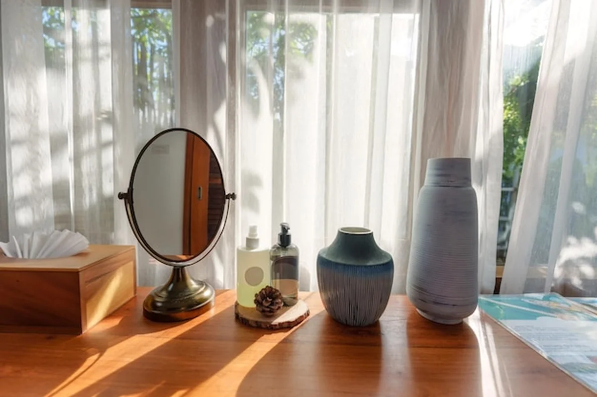 Toaletka z lustrzanym kremowym wazonem i pudełkiem na chusteczki przy białej zasłonie