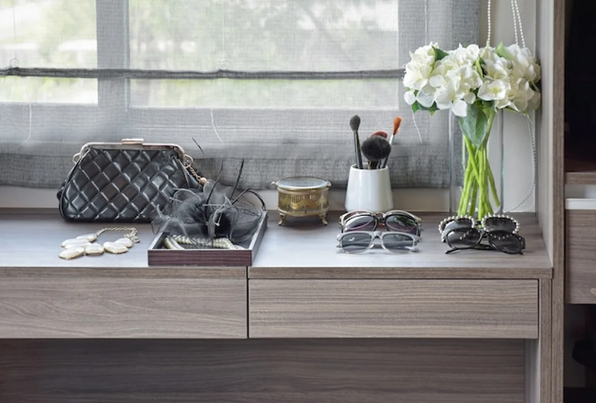 Torebka, okulary przeciwsłoneczne, biżuteria i pędzle do makijażu na drewnianej toalecie
