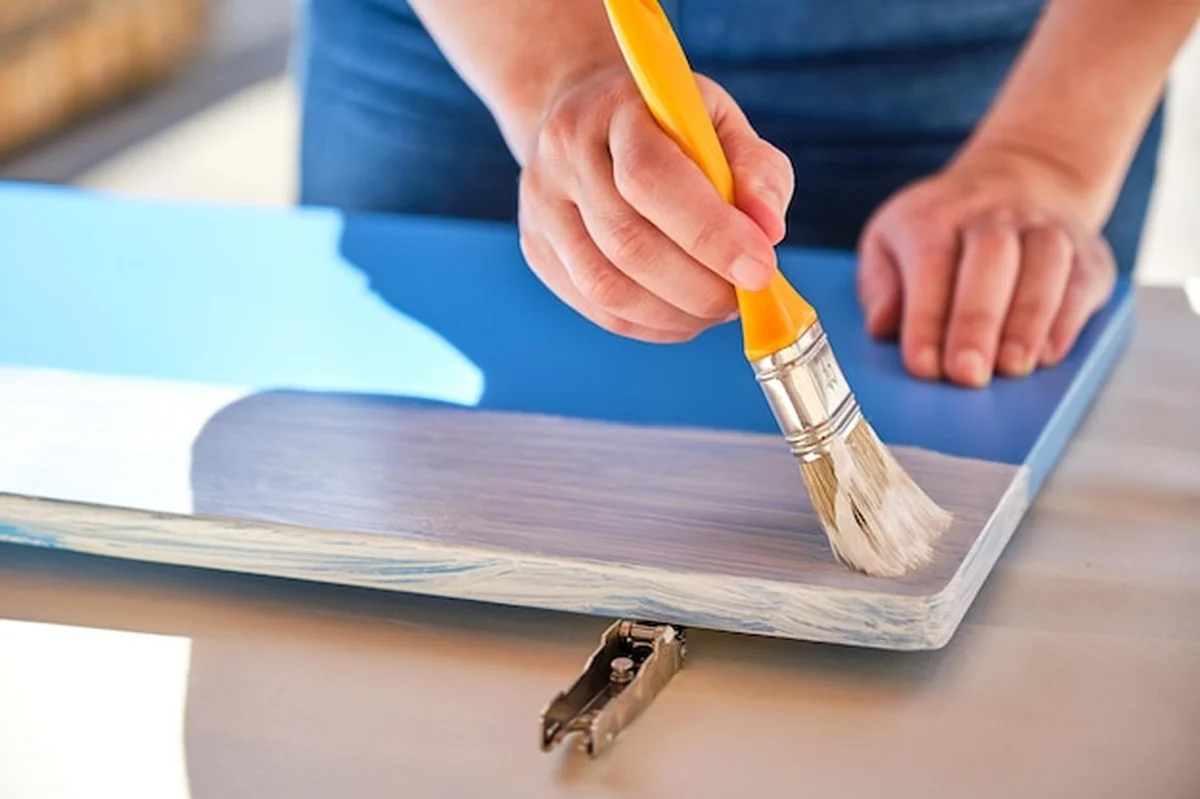 Kobieta maluje niebieskie meble białą farbą