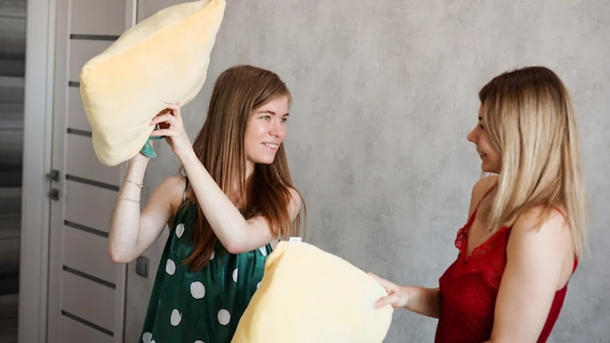 Dwie koleżanki walczą na poduszki w pokoju na piżamowej imprezie