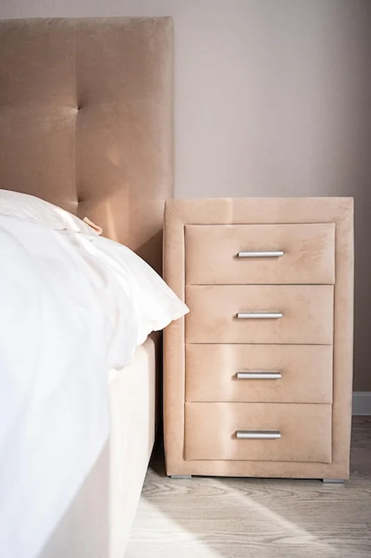 Beżowa szafka z czterema szufladami obok łóżka w naturalnym świetle